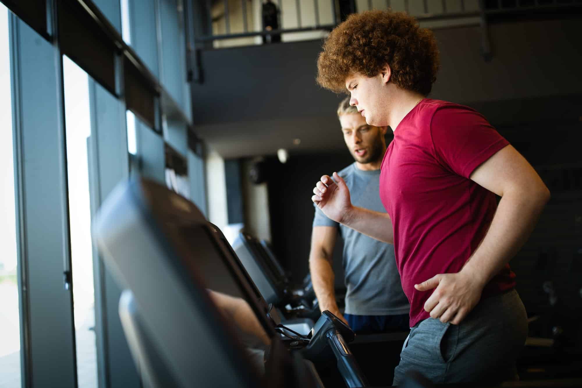 Overweight young man exercising gym with personal trainer